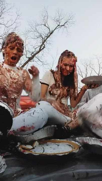 Two girls wearing all white have a food fight in the bed of a pickup truck