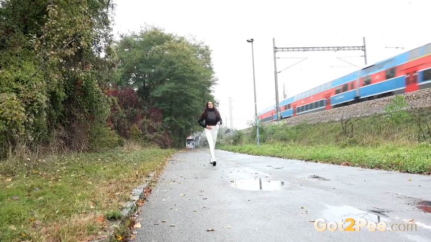 Maddi Black pees into a puddle on a road next to the railway line